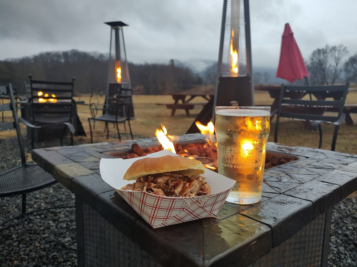 A BBQ Beast pulled-pork sandwich and a pint of Blue Toad cider beside the fire pit at the farm